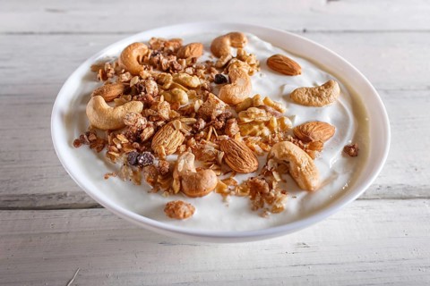 White plate with greek yogurt, granola, almond, cashew, walnuts on white wooden background. close