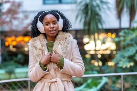 Stylish young woman enjoying a winter day in the city, wearing earmuffs and a chic winter coat,