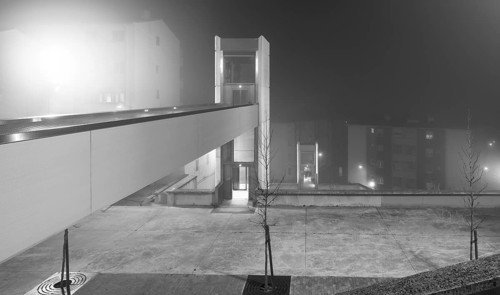 A eerie urban evening captured with a fog enveloped elevator and an overhead walkway connecting