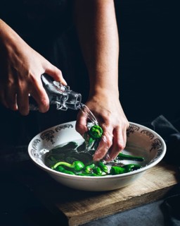 Hands gently wash fresh green peppers in a decorative bowl, under a stream of water from a bottle,