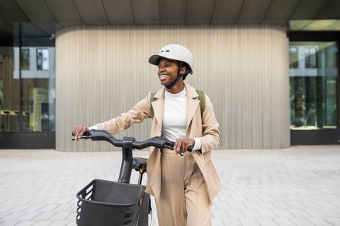 Black woman in a stylish outfit rides an electric bike in a cityscape Helmet on, with a confident