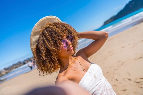 Personal perspective of a beauty latin woman with sunglasses and hat taking selfie at the beach