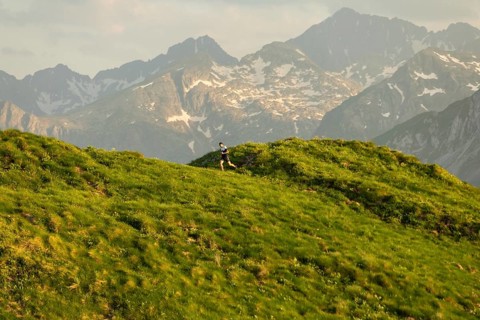A lone runner is captured mid-stride on a lush green trail with majestic mountains in the