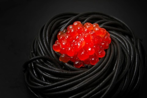 Black spaghetti with red caviar, pasta, on a black background, top view, no people