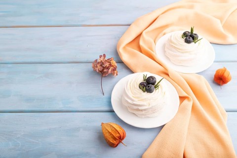 Pavlova Meringue dessert with crisp meringue and blueberry on blue wooden background with orange