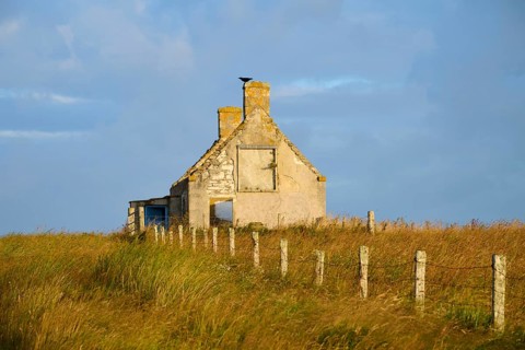 An abandoned stone house with fence stands in a vast meadow under a partly cloudy sky, Moine House,