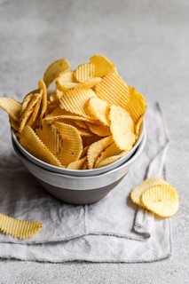 A bowl of crispy homemade potato chips served on a rustic fabric napkin. These golden, wavy chips