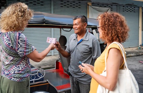 A Thai tuk tuk driver in Chiang Rai joyfully accepts payment from a female tourist, while another