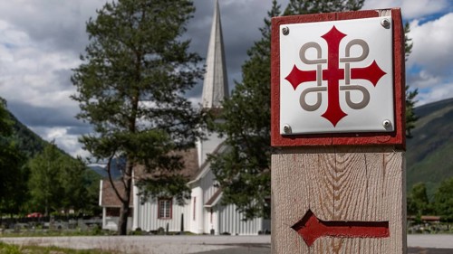 Waymarker Olav's cross for pilgrims, Sel church or Sel kyrkje in the background, Olavsweg or