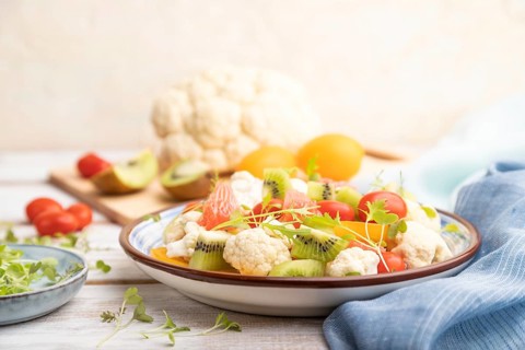 Vegetarian salad of cauliflower cabbage, kiwi, tomatoes, microgreen sprouts on white wooden