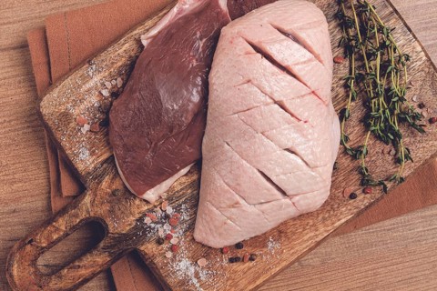Fresh raw duck breasts, on a wooden chopping board, with herbs and spices, no people
