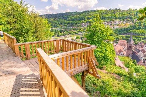 Wooden platform with a view of a cityscape surrounded by green forests, panoramic wooden walkway,