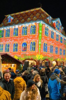 An impressive building with a colourful light projection attracts a large crowd at night, Christmas