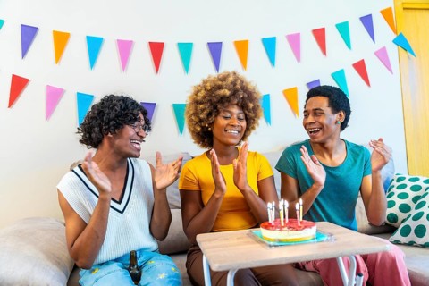 Three multiracial males and female friends singing and clasping hands celebrating birthday at home