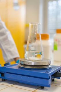 A flask with liquid sits on a blue hotplate in the laboratory, Nagold Youth Research Centre, Black