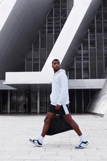 A confident black male athlete is captured in motion, wearing a hoodie and shorts in an urban
