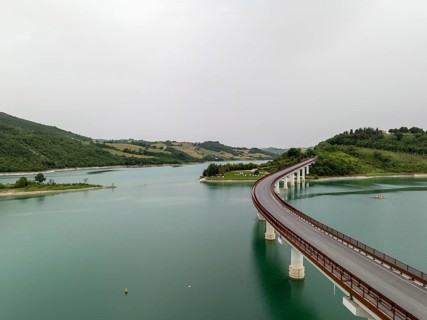 Aerial view of the scenic curved bridge spanning Castreccioni Lake in Italy. Calm turquoise waters