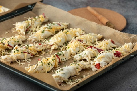 Dough rolls sprinkled with cheese and herbs on baking paper, ready for baking