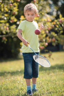 Six years old boy play with racket and ball in the garden