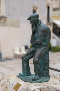 Bronze sculpture of a pensive man sitting on a stone in a historic city centre setting, Matera,