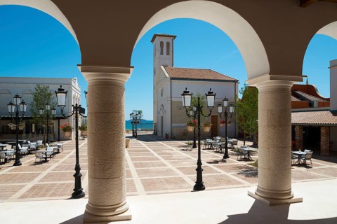 View through arches to a sunlit square with a church in the background, Amadria Park, Sibenik,