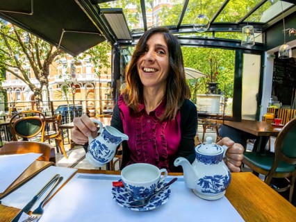 Happy woman pouring milk into her teacup, enjoying a relaxing moment at an outdoor cafe in london