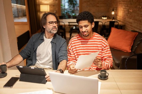 Two professionals collaborate in a cozy coworking space, surrounded by laptops, tablets, and coffee