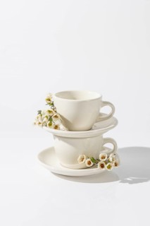 Stacked white ceramic tea cups with delicate spring flowers adorning the side, set against a clean,