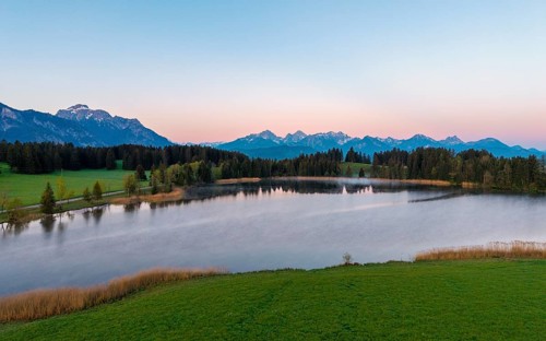 A calm lake in the morning light, surrounded by mountains and green forest, Hergratsrieder See,
