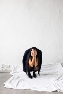 A joyful Asian woman is playfully crouching, wearing an oversized jacket. She expresses exuberance
