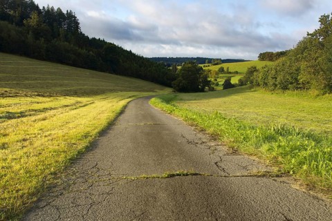 Wide tarmac path leads through green fields and forests under a cloudy sky, Siegen, North