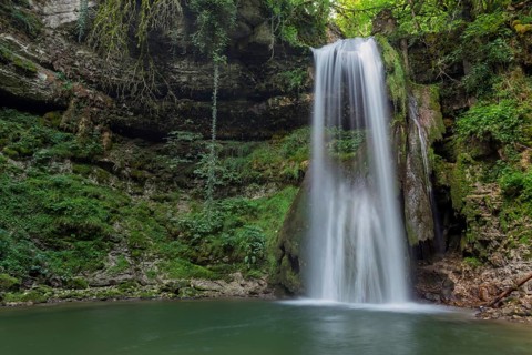 A waterfall flows into a small pool of water. The water is clear and the rocks are scattered around