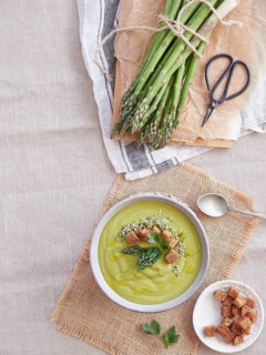 Bunch of freshly picked green wild asparagus on the table next to creamy soup with pieces of