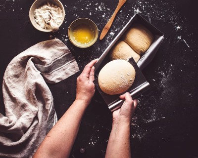 Hands preparing homemade sliced bread by placing dough into a baking pan on a flour dusted counter.