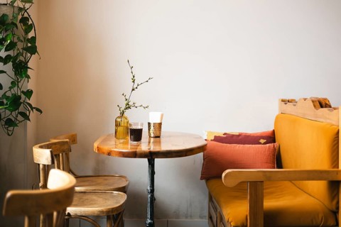 A cozy cafe corner featuring a rustic wooden table, chairs, and a cushioned bench. The warm decor