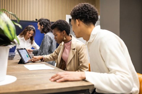 A diverse group of colleagues engage in teamwork in a modern office. They focus on digital tablets