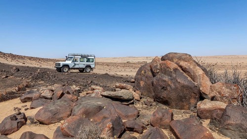 White off-road vehicle in desert-like landscape with large rocks and clear blue sky, Namib-Naukluft