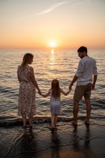 A family stands barefoot on the shore of an Italian beach, holding hands as they watch the sun set