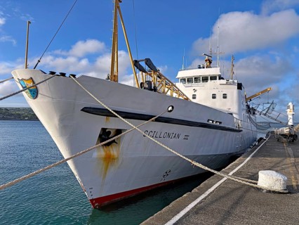 A large ship is moored at the quay with ropes, surrounded by sea and sky under a slightly cloudy