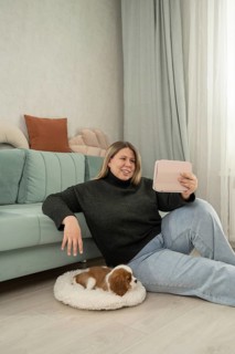 Woman relaxing at home with her adorable puppy resting nearby. She enjoys digital content on her