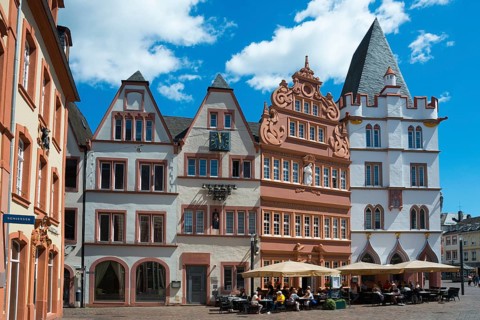 Historic half-timbered houses on a lively square with outdoor seating under a blue sky,