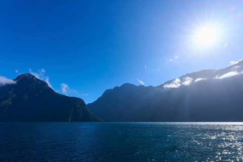 Clear blue fjord landscape with sun over mountains and water, summer, Milford Sound, Te Anau,