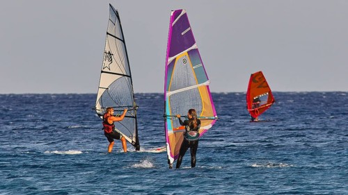 Three windsurfers navigating over the blue sea under clear skies, windsurfing, Meltemi windsurfing