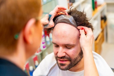 Close-up top view of a hairdresser attaching a capillary prosthesis carefully to a man's head
