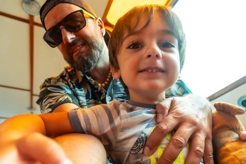 A man and a boy are sitting together, the man is wearing sunglasses and the boy is smiling
