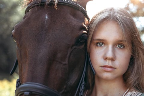 Close up portrait of a young girl beside a brown horse, capturing a serene moment in a natural