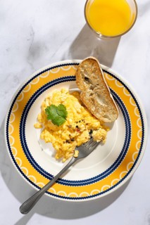 A colorful breakfast setting featuring fluffy scrambled eggs garnished with herbs, served with a