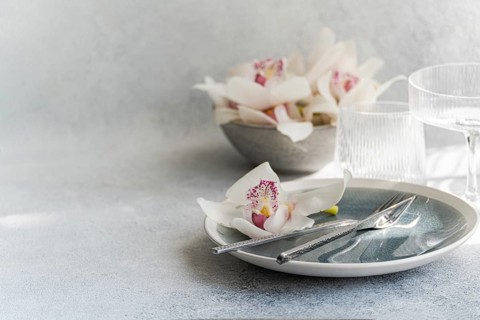 A serene table setting featuring delicate orchids on a pastel plate, accompanied by silver cutlery