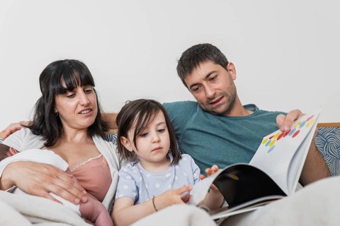 A young family enjoys quality time, with the big sister reading a storybook while the parents and