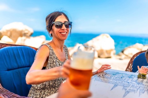 Woman toasting with a glass of beer at a seaside restaurant in piran, slovenia, enjoying a sunny